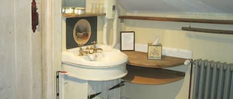 A compact bathroom with a white sink, a mirror, and a wooden shelf above it.