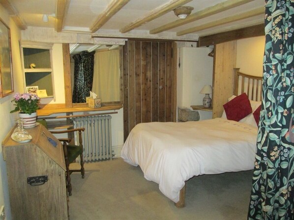 A bedroom with a wooden bed, a desk with a chair, a radiator, and a window with curtains.
