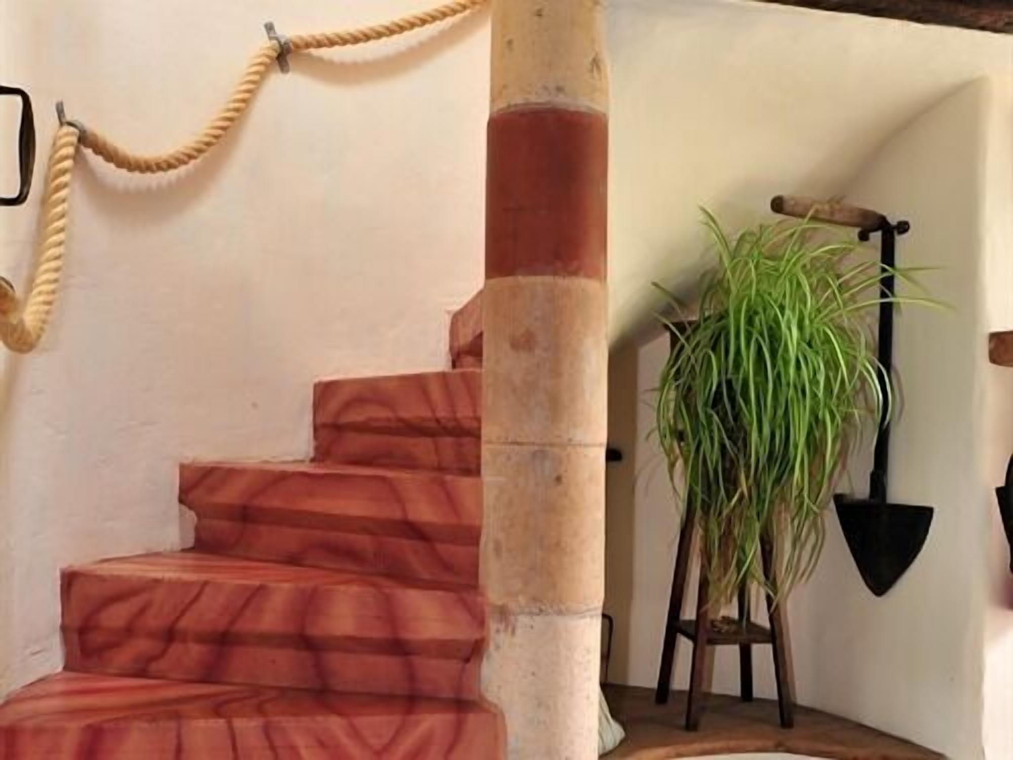Un escalier avec une barrière faite de cordes, un pot de fleurs et une pelle accrochée au mur.
