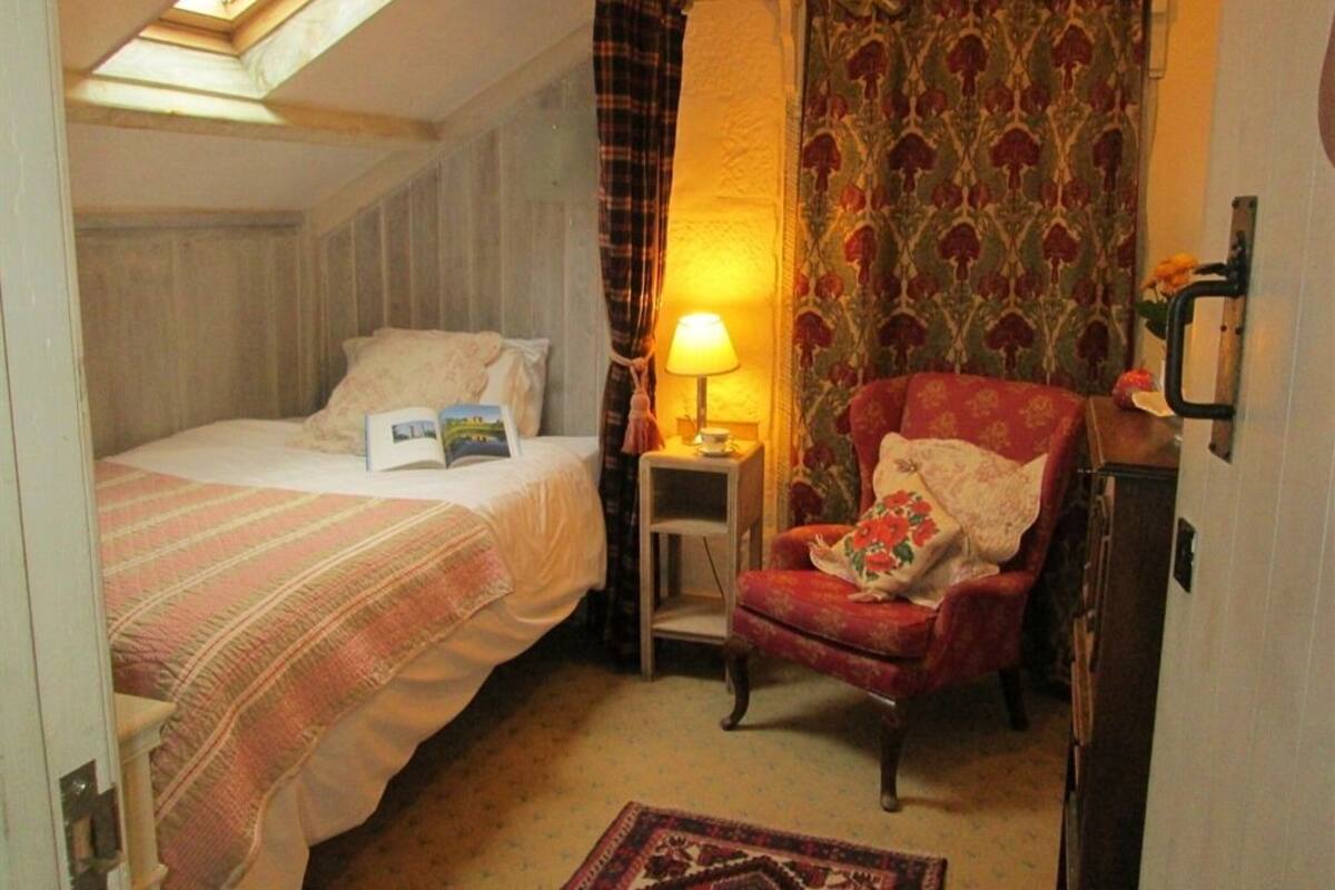 Um quarto aconchegante com uma cama, uma cadeira, uma mesinha de cabeceira e uma luminária.