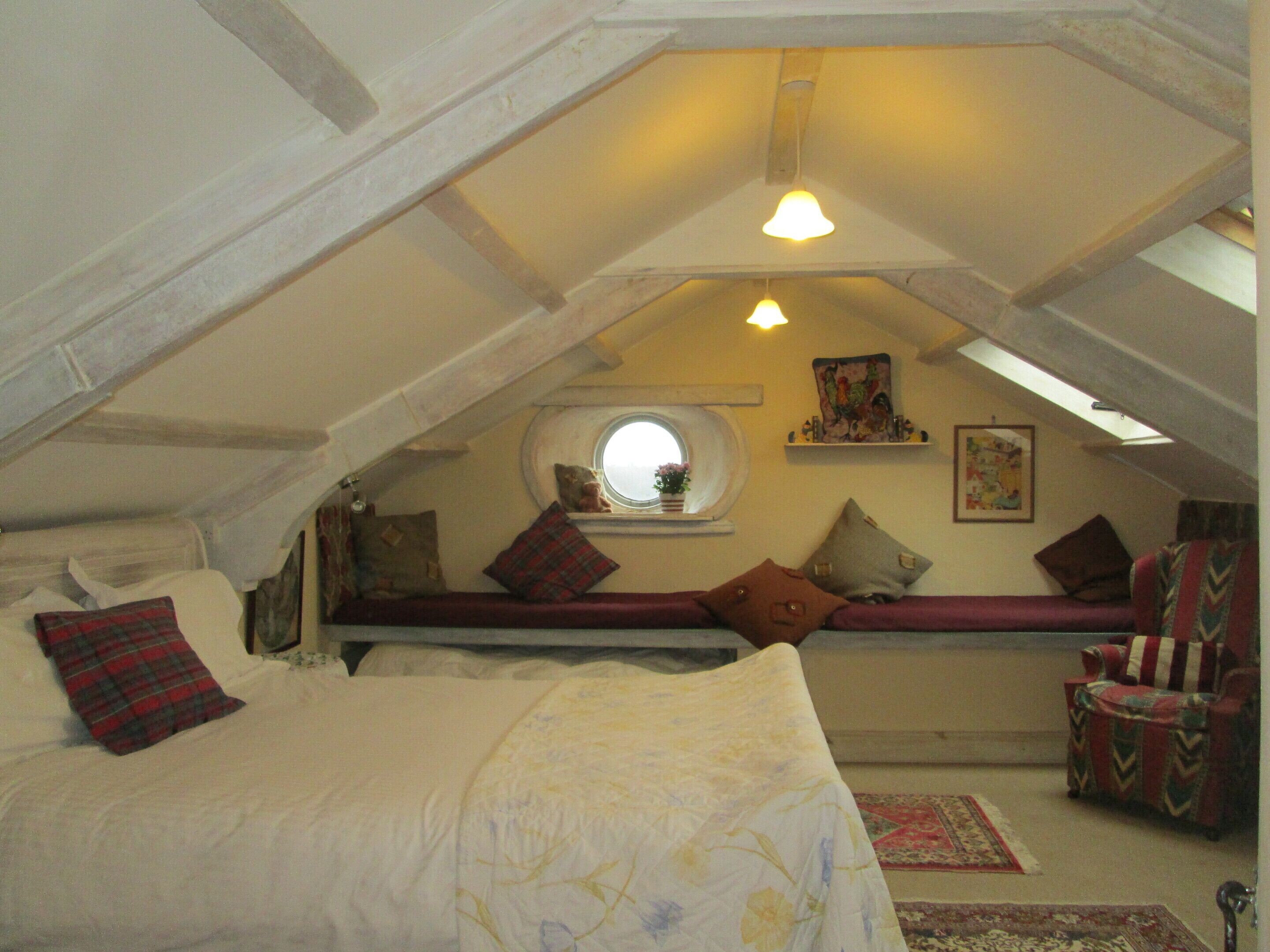 Een gezellig slaapkamer op zolder met een schuine plafond, een raam, een bed met kussens, een stoel en een vloerkleed.