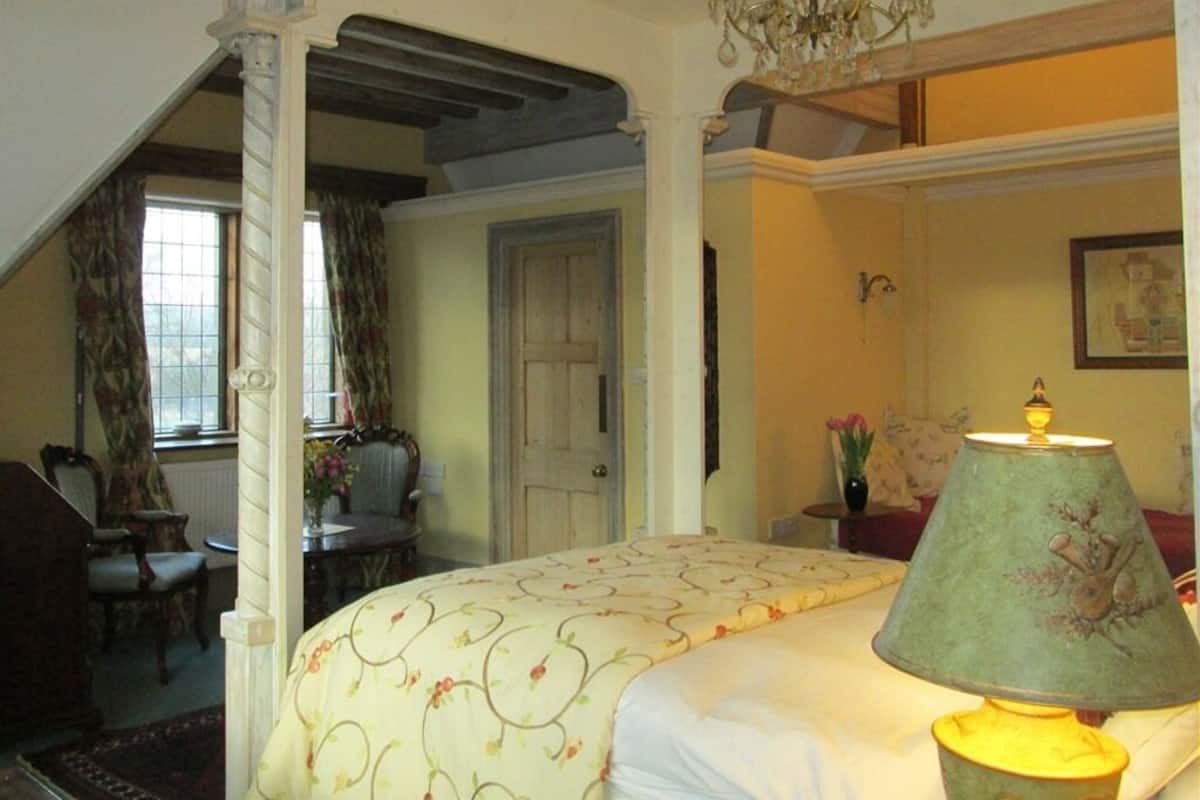 Um quarto com cama, um lustre, um abajur e uma janela com cortinas.