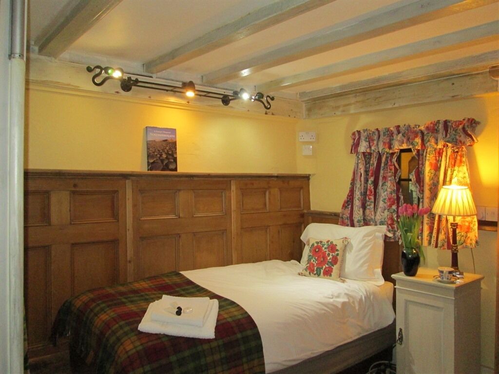 A neatly made bed with a plaid blanket, a wooden headboard, a bedside lamp, and a floral curtain.