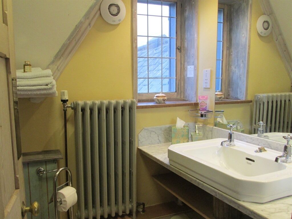 Een badkamer met een groot wastafel, een spiegel, een raam en een radiator.
