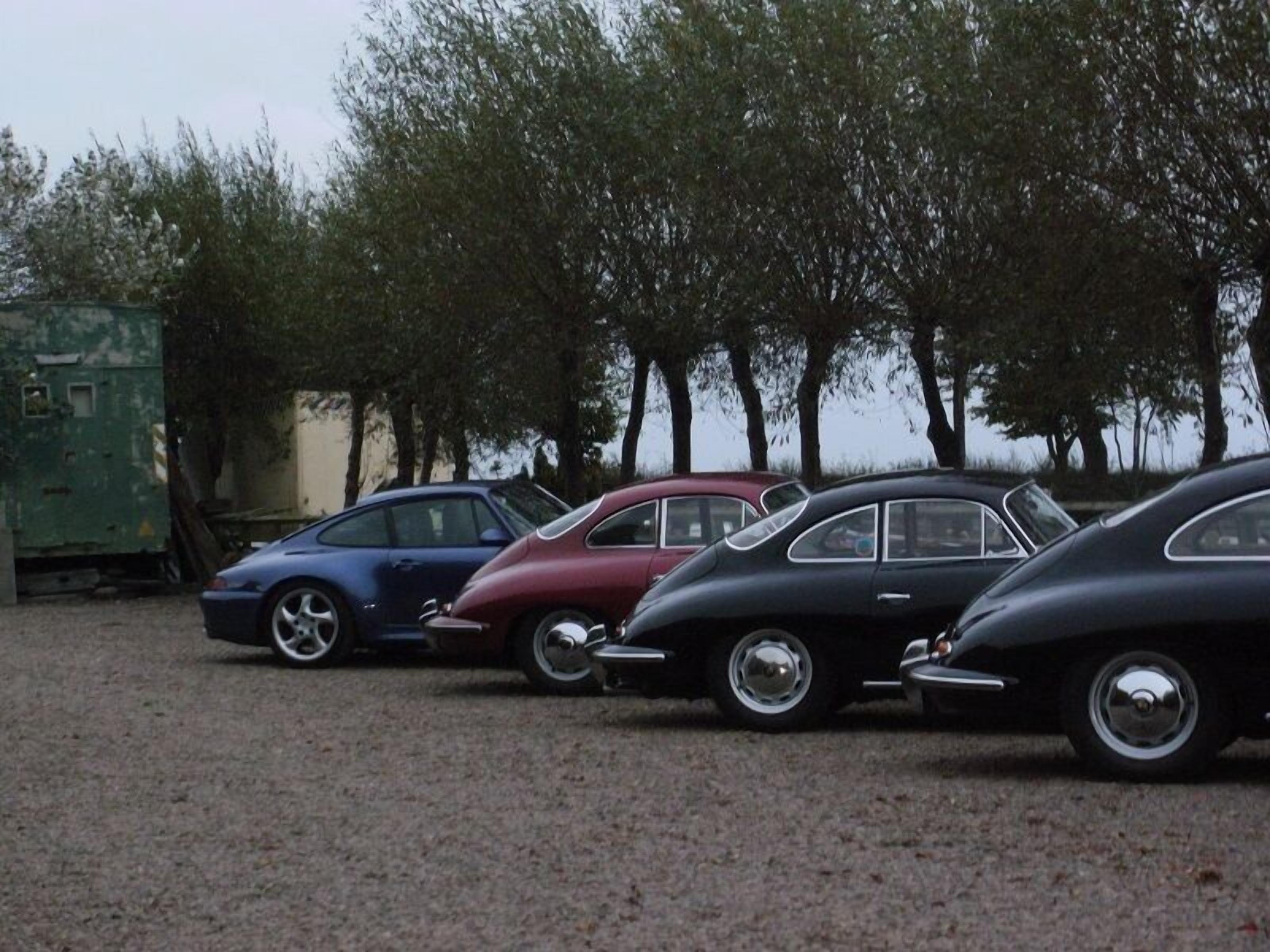 Uma fileira de carros antigos estacionados em um estacionamento, com árvores ao fundo.