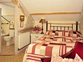 A bedroom with a bed, a nightstand, a lamp, a radiator, and a bathroom visible through an open door.