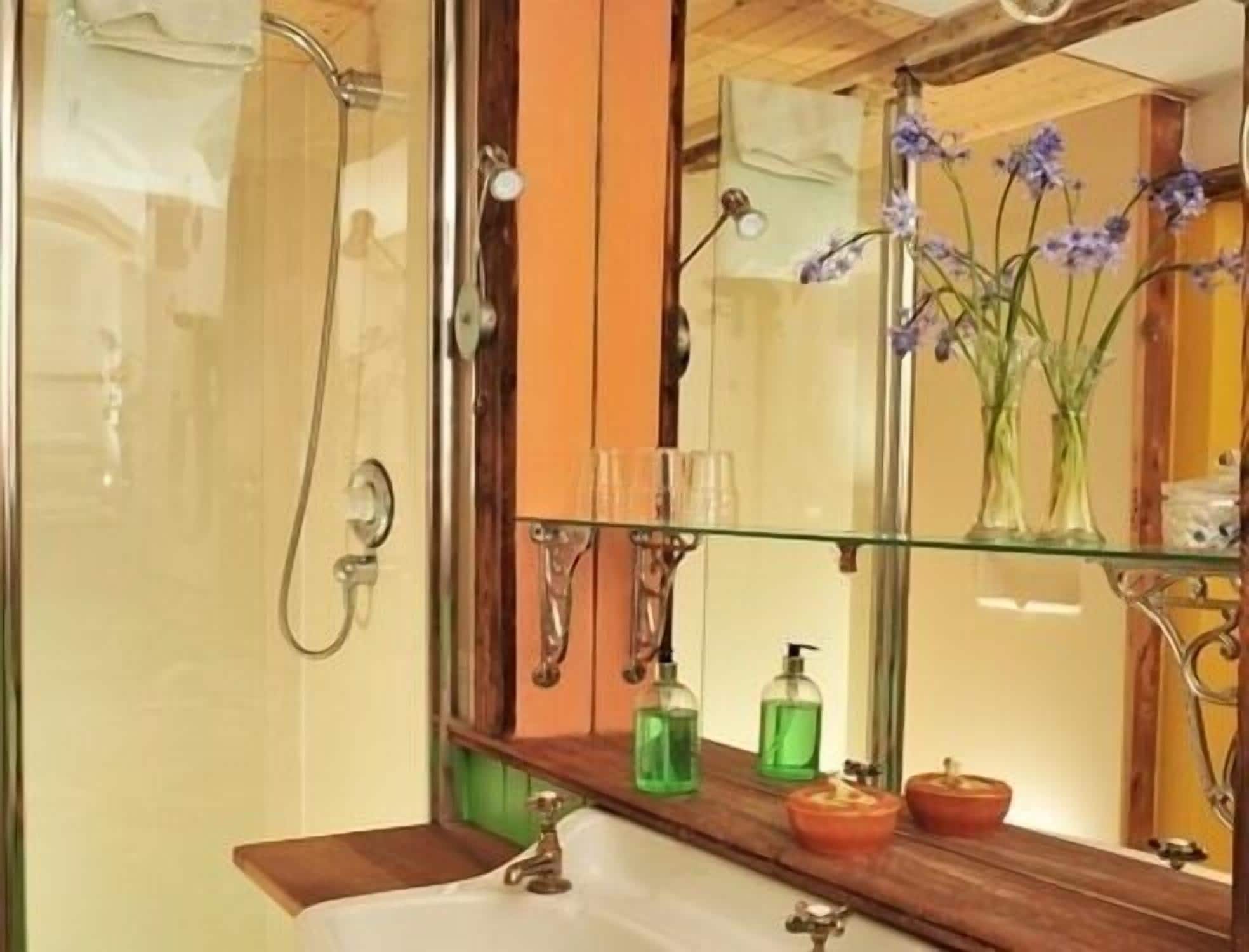 A bathroom with a glass shower enclosure, a wooden vanity, and a mirror reflecting a vase with flowers.