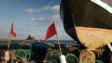 Een boot met een rode vlag, omringd door groene vistuigen en drijvers op het strand.