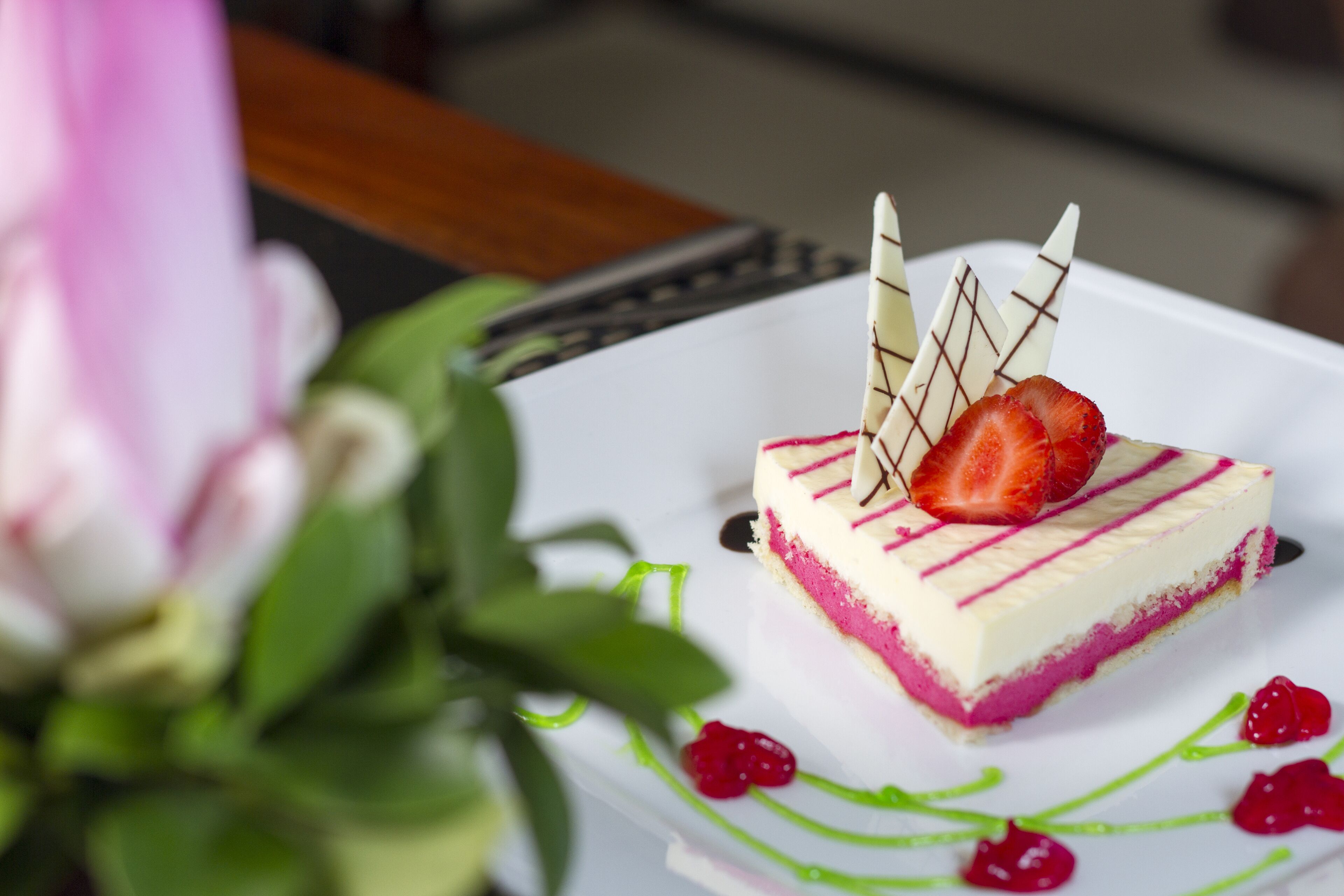 A dessert with a strawberry on top, surrounded by green leaves.