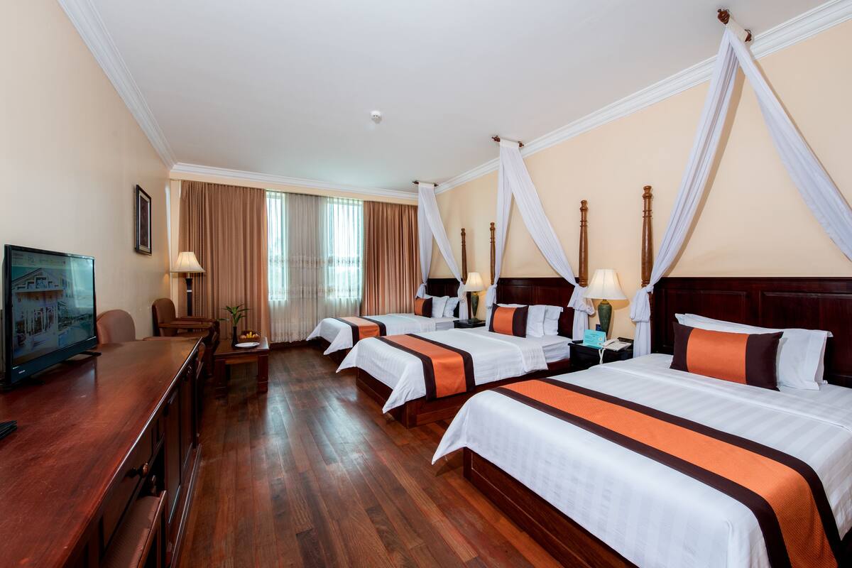 Quarto de hotel com quatro camas, piso de madeira, televisão e uma mesa.