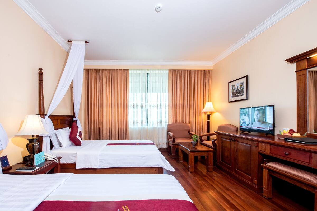Quarto de hotel com duas camas, televisão, escrivaninha e uma cadeira.