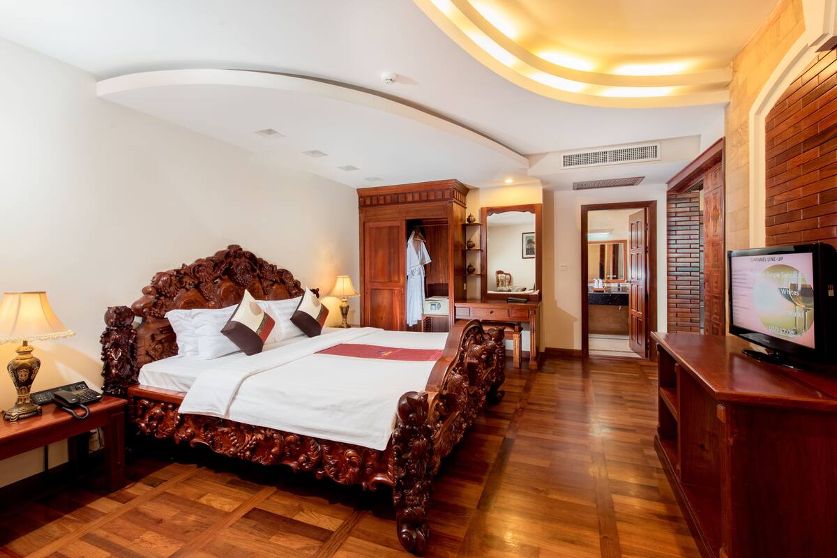 Um quarto de hotel espaçoso com uma cama de madeira grande, uma televisão e um guarda-roupa de madeira.