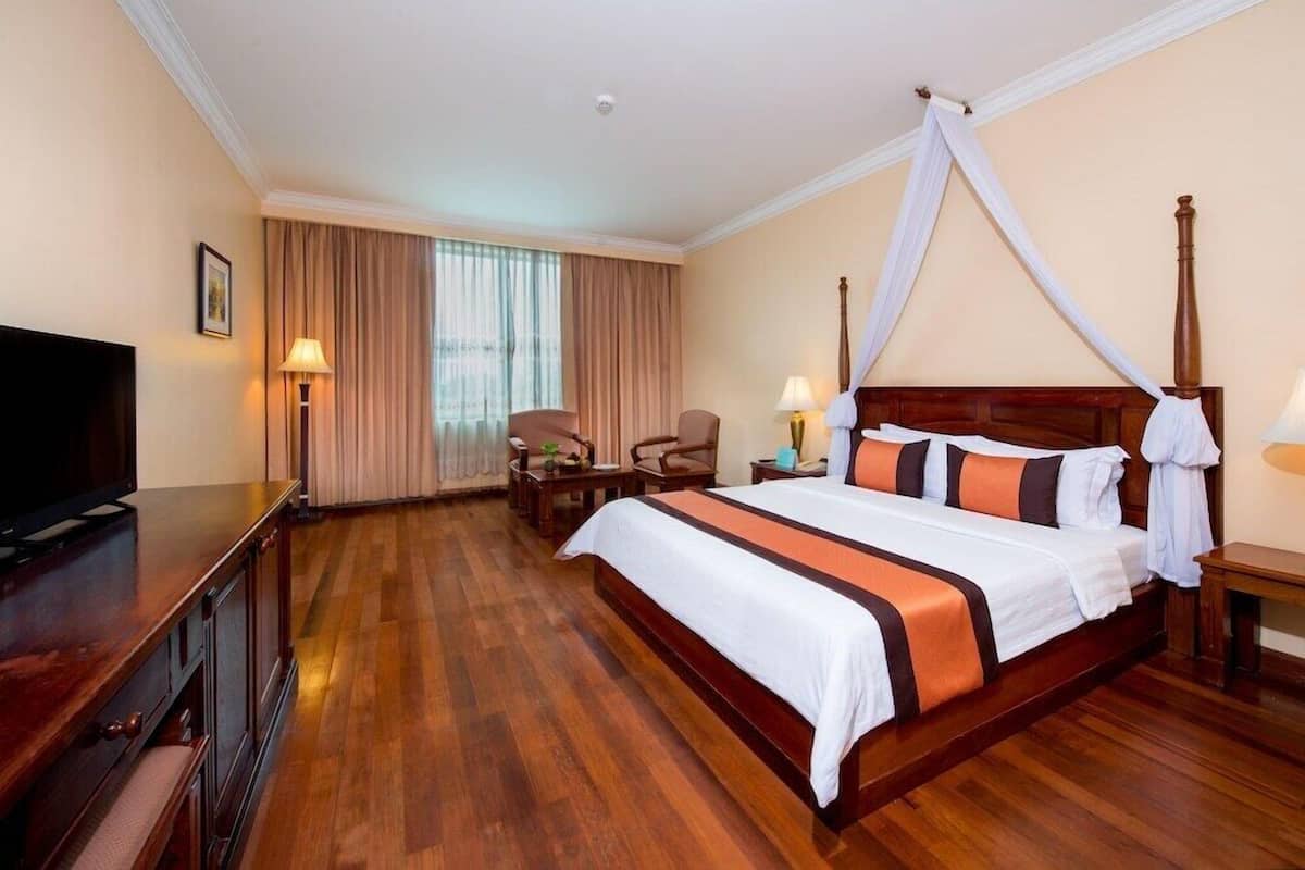 Quarto de hotel com uma cama grande, televisão, escrivaninha e cadeira.
