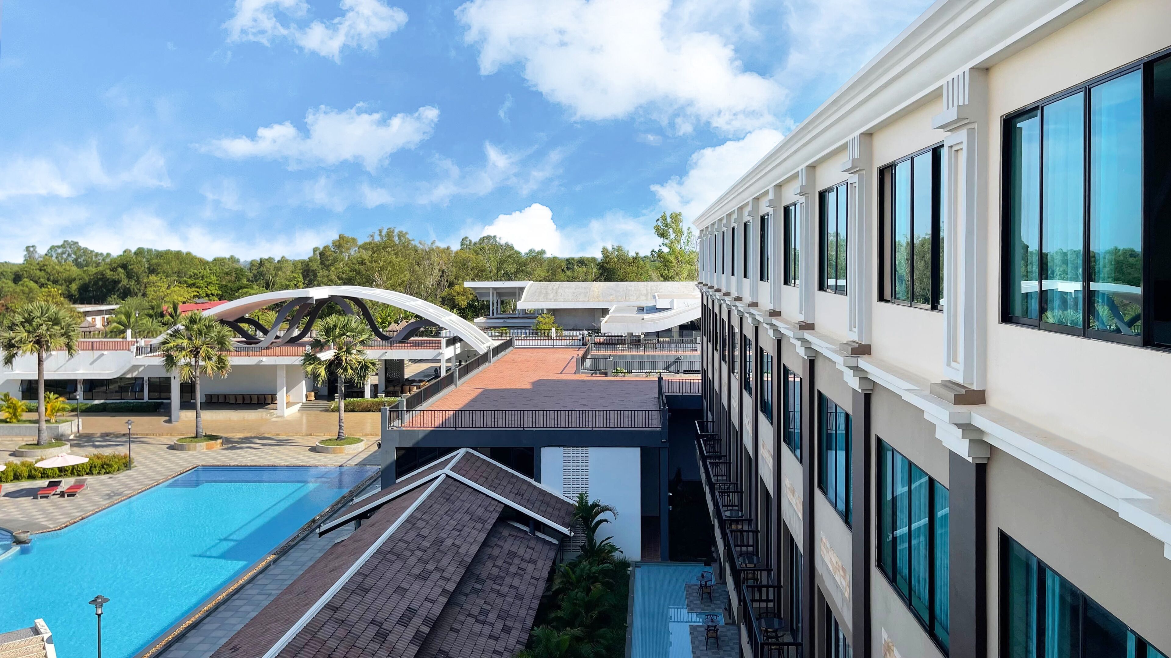 Um hotel com piscina, área externa coberta e um edifício moderno com grandes janelas.
