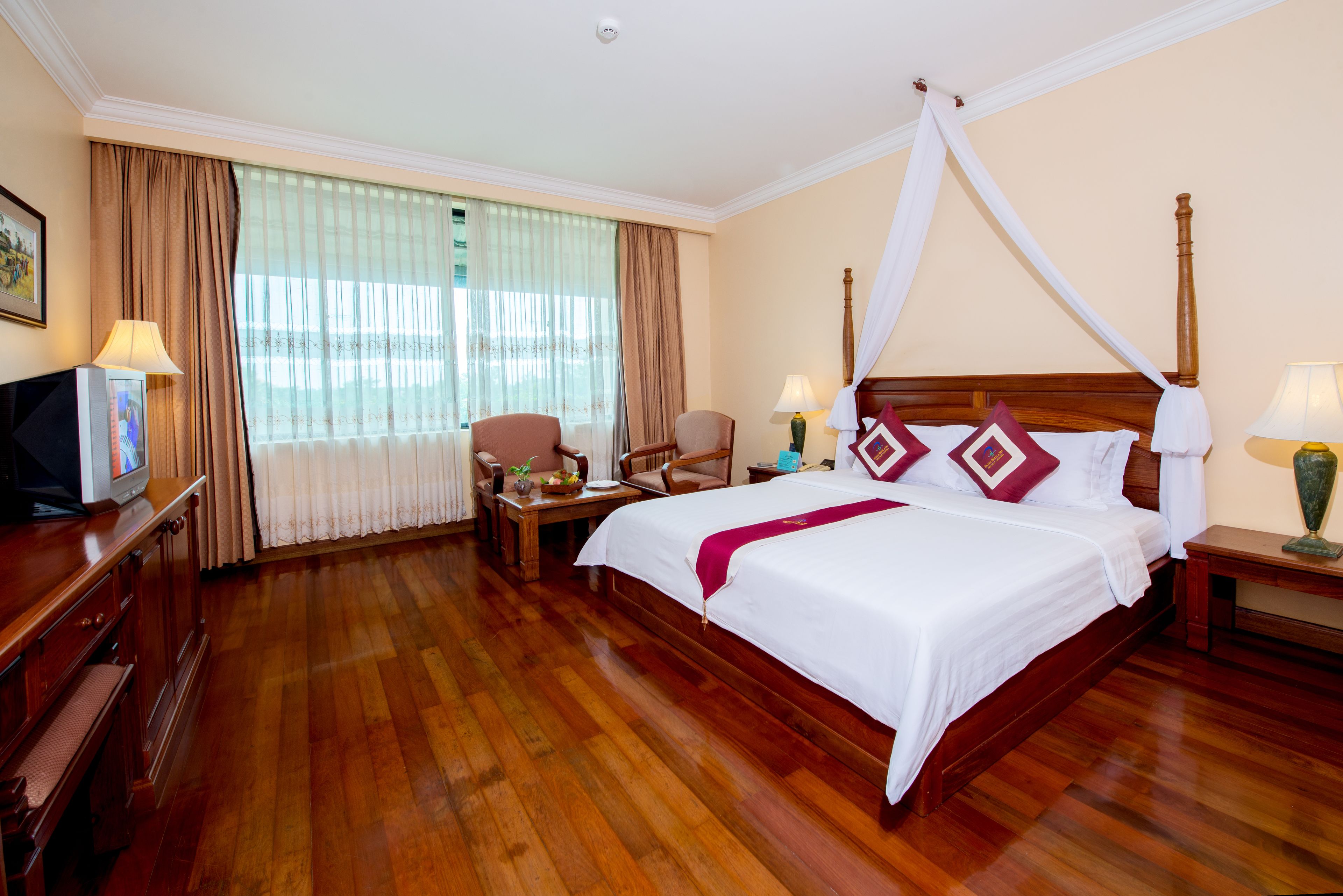 A hotel room with a large bed, wooden flooring, a desk with a television, and a chair.