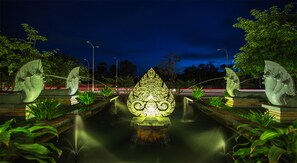 A nighttime view of a water feature with a central sculpture, surrounded by greenery and illuminated by street lights. - Pacific Hotel & Spa (Siem Reap)