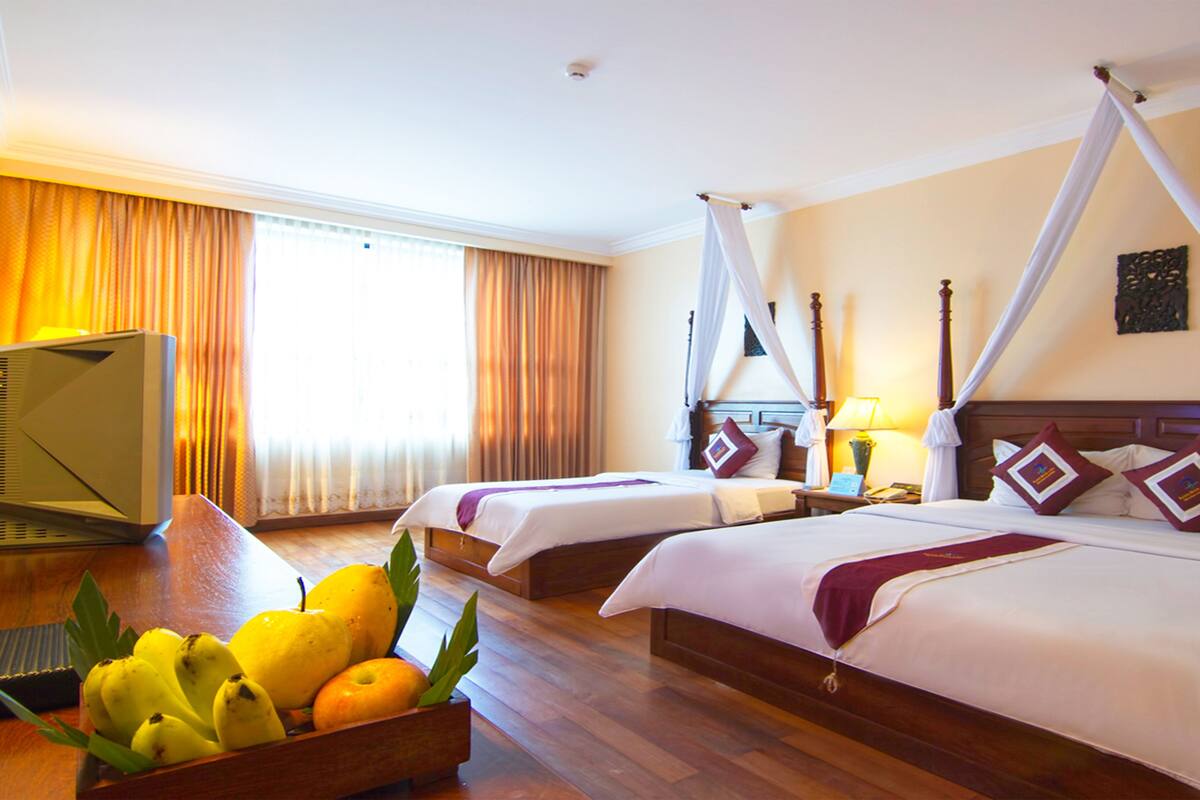 Quarto de hotel com duas camas, televisão e uma cesta de frutas.