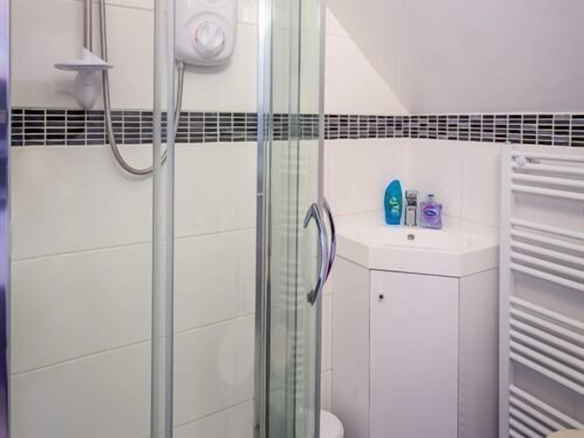 A bathroom with a glass shower enclosure, a white sink with toiletries, and a towel rack.