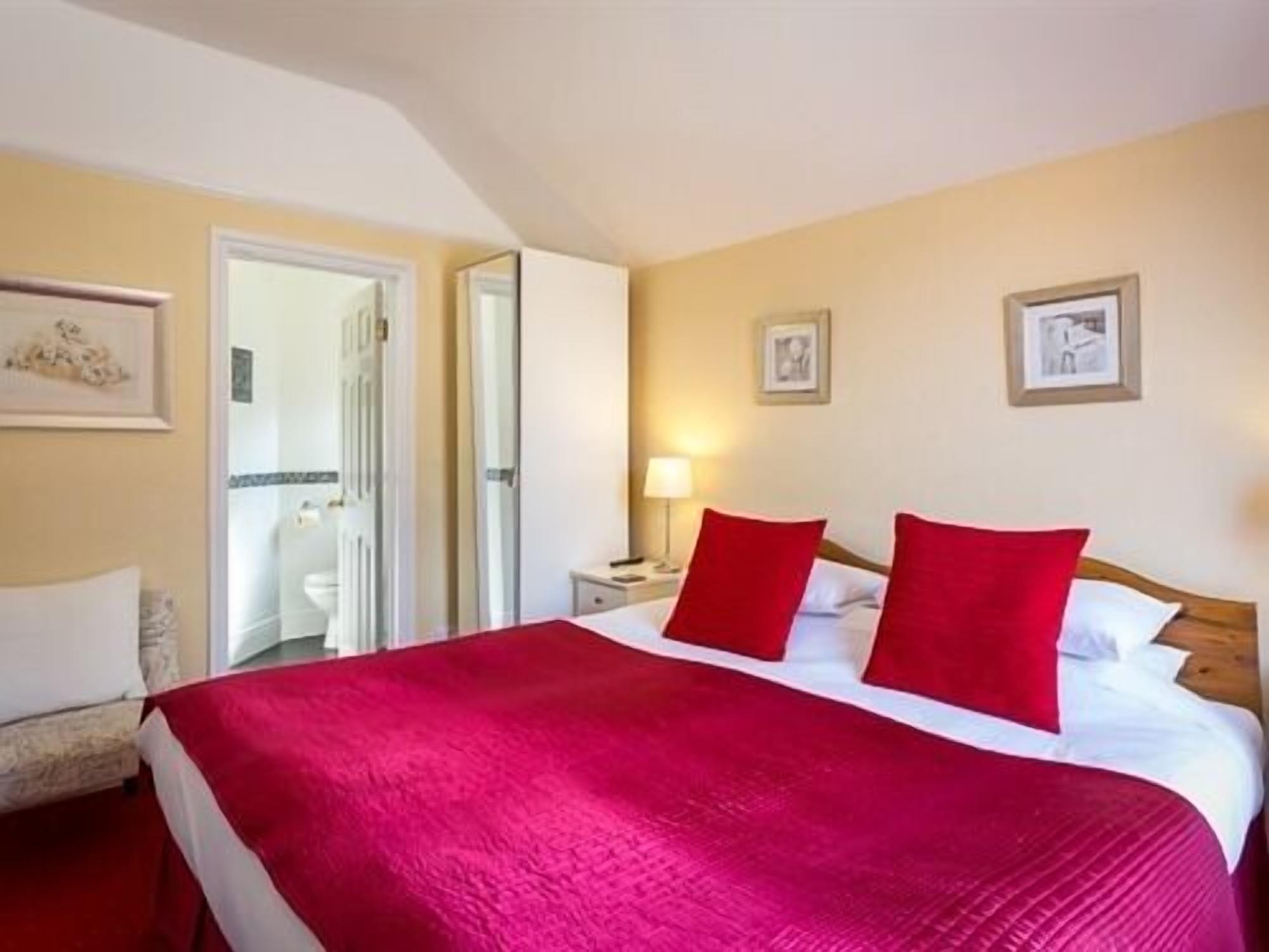 A hotel room with a large bed, red pillows, a bedside table with a lamp, and framed pictures on the wall.