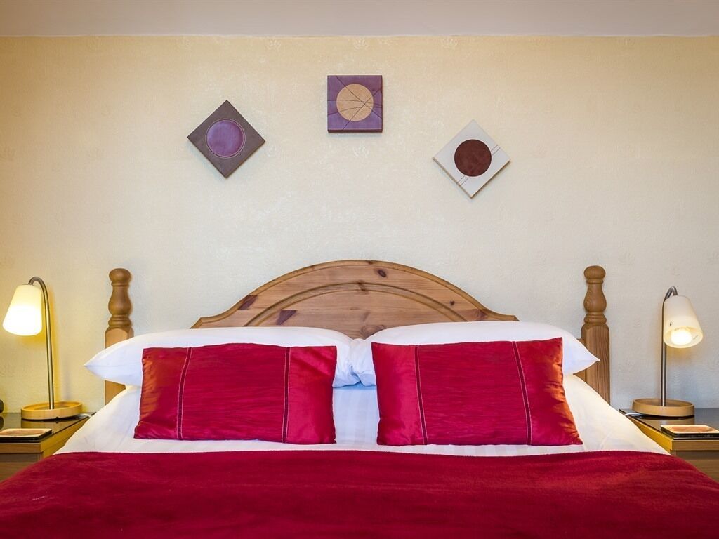 Ein Hotelzimmer mit einem Holzkopfteil, einer roten Bettdecke und zwei Nachttischlampen.