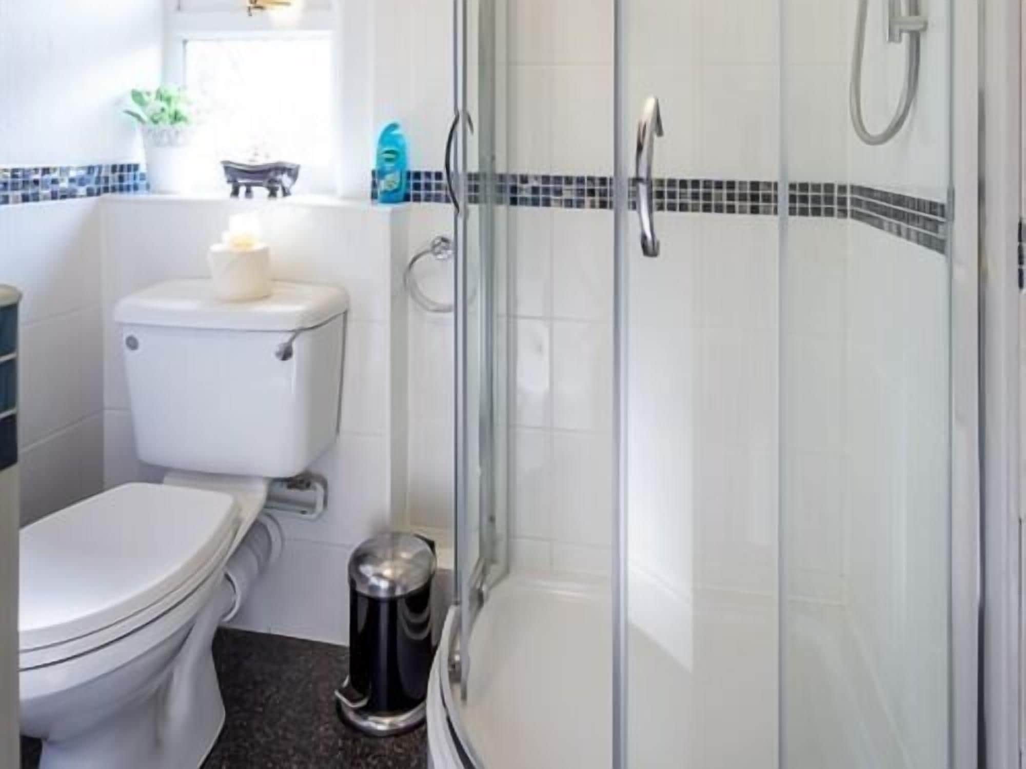 Een badkamer met toilet, een bidet, een douche met glazen wanden en een prullenbak.