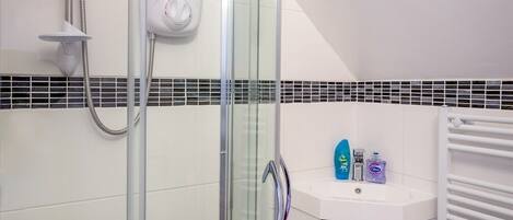 Une salle de bain moderne avec une douche à l’italienne en verre, un lavabo blanc agrémenté d’articles de toilette et un mur recouvert de carreaux.