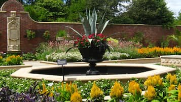 A garden with a central fountain, surrounded by various flower beds and a brick wall.