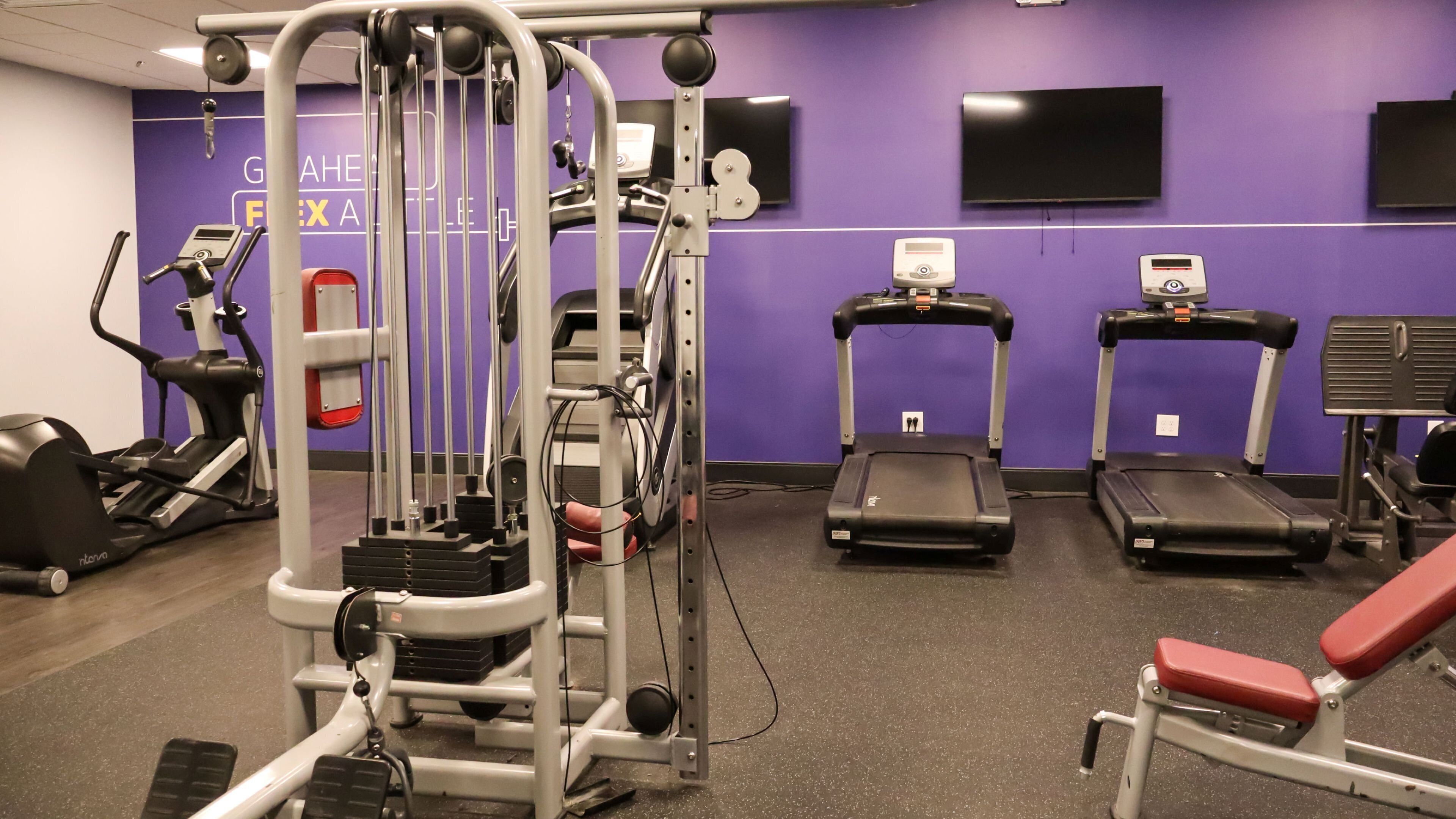 A gym with various exercise equipment including treadmills, an elliptical, and a weight machine.