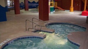 An indoor swimming pool with two hot tubs, a safety ladder, and a no diving sign. - Holiday Inn Omaha Downtown - Waterpark by IHG (Omaha)