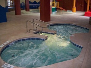 Piscina interna com duas banheiras de hidromassagem, uma escada de segurança e aviso de proibição de mergulho.