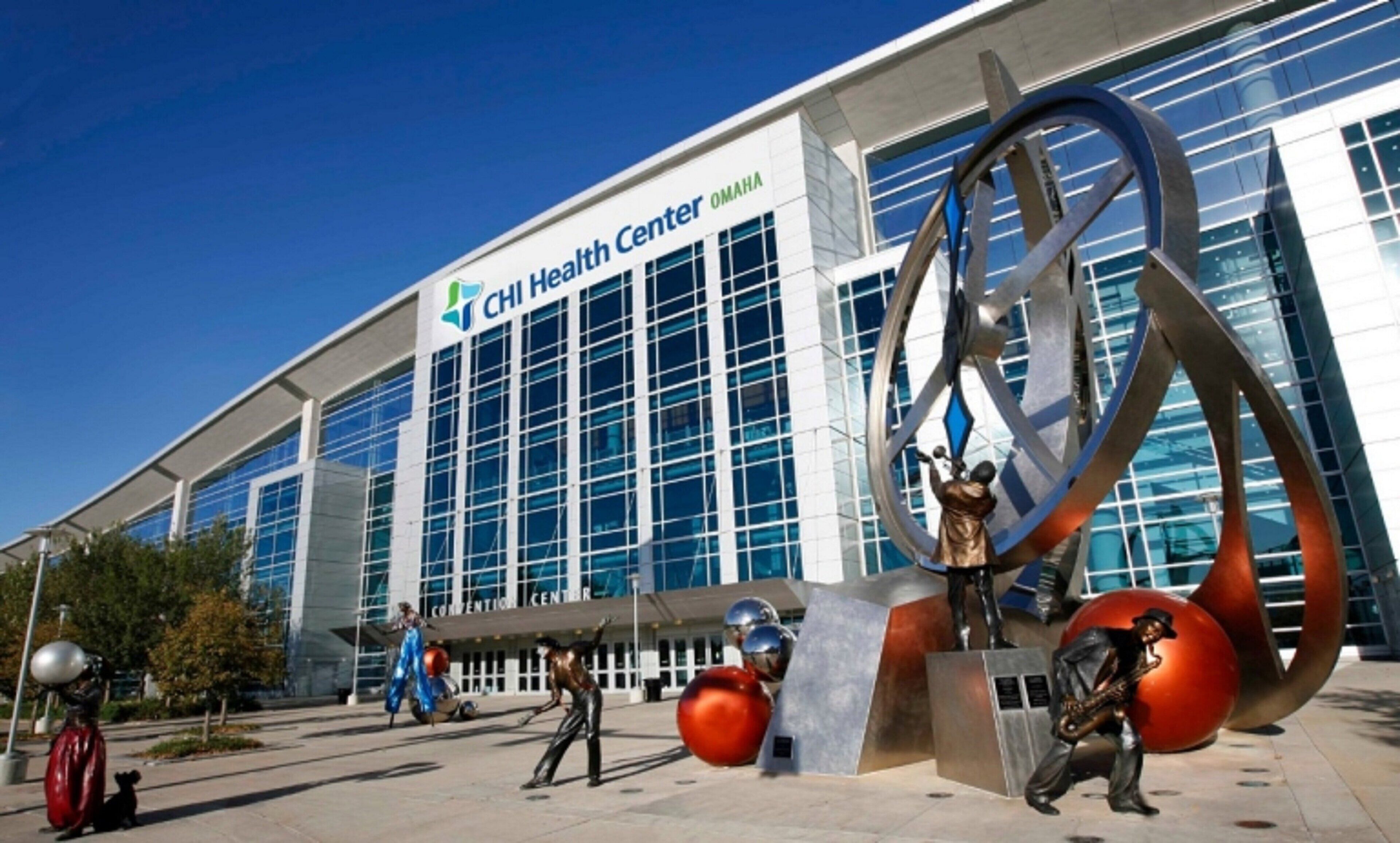 A modern building with a large glass facade, a prominent sign reading 'CHI Health Center Omaha,' and a sculpture of a figure with a raised arm.