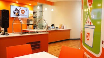Un espace proposant des yaourts glacés en libre-service, avec un système de paiement sans espèces, un menu numérique et un coin salon doté de chaises orange et d’une table blanche.