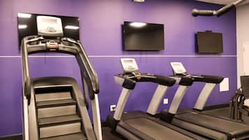 Une salle de sport avec des tapis de course et un appareil d’escalier, le tout adossé à un mur violet, avec un téléviseur fixé au-dessus.
