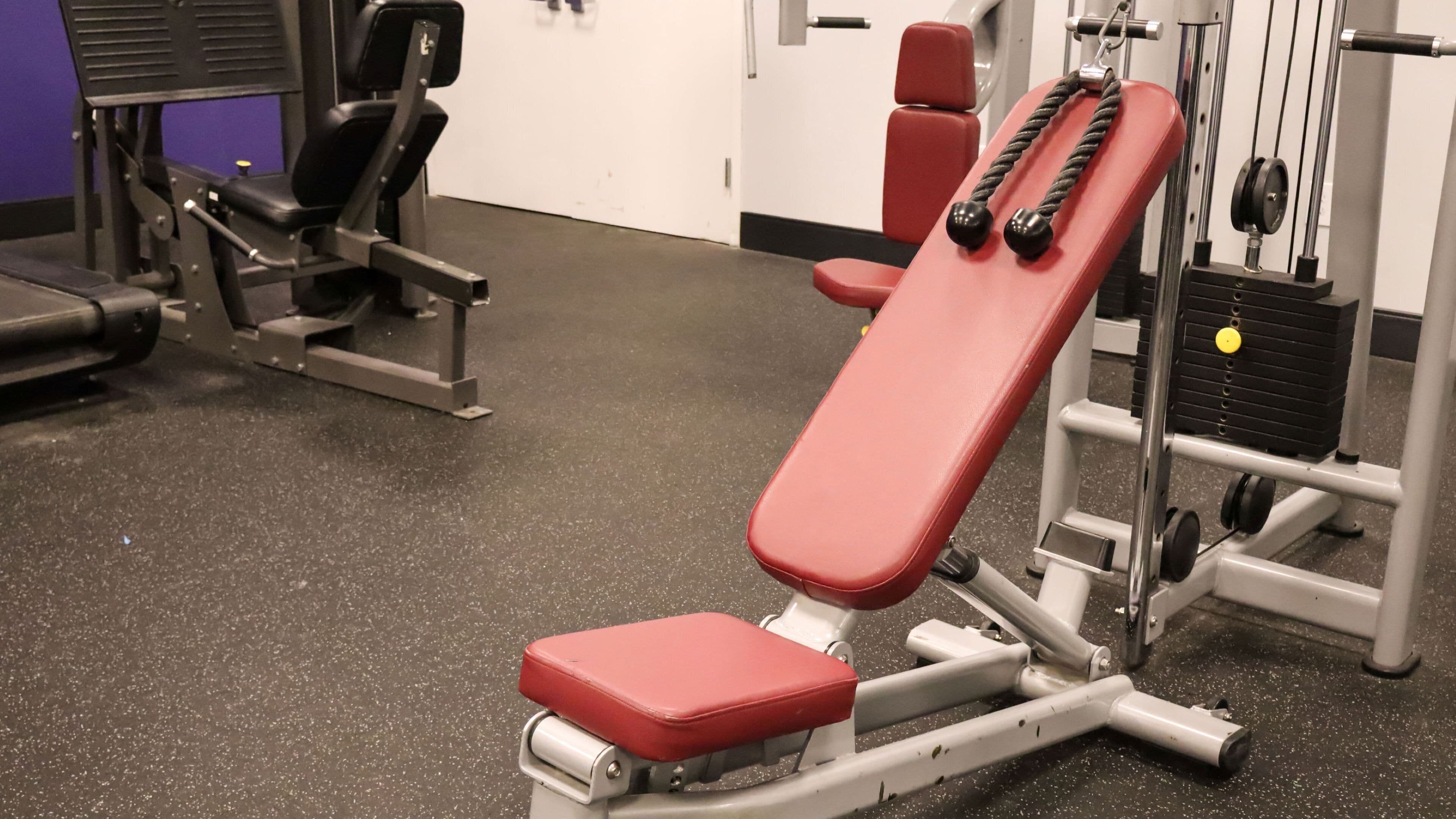 A gym with a red bench, weight machines, and a black cable machine.