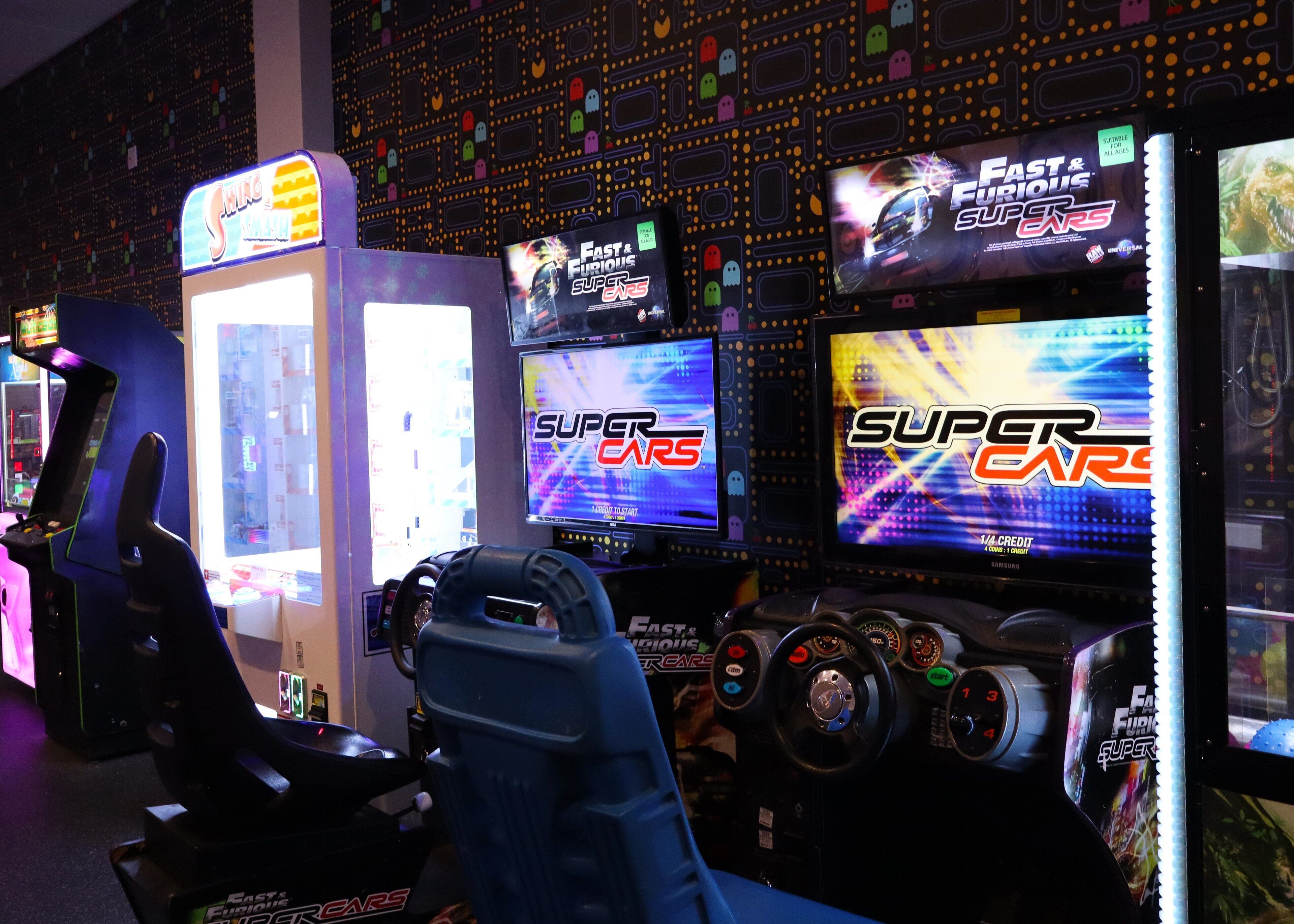 Una hilera de juegos de carreras de arcade con la marca 'Fast & Furious', un volante y un asiento de carreras.