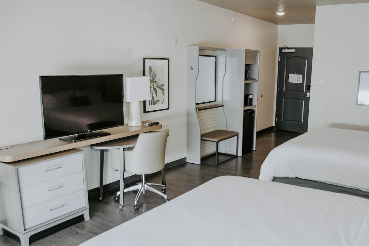 Habitación de hotel con escritorio, silla, televisión y dos camas.