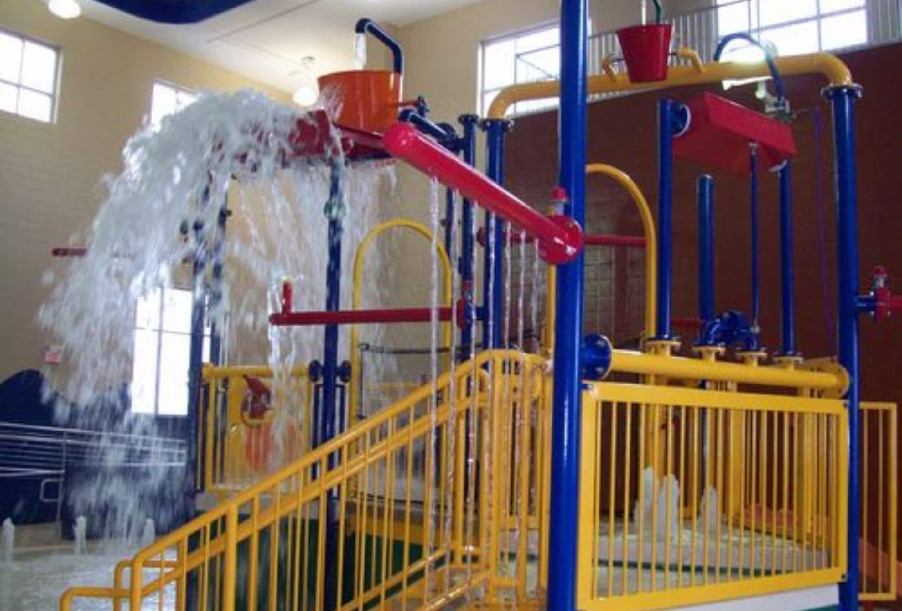 Un espace de jeux aquatiques avec des structures jaunes et bleues, comprenant un toboggan et une fontaine.