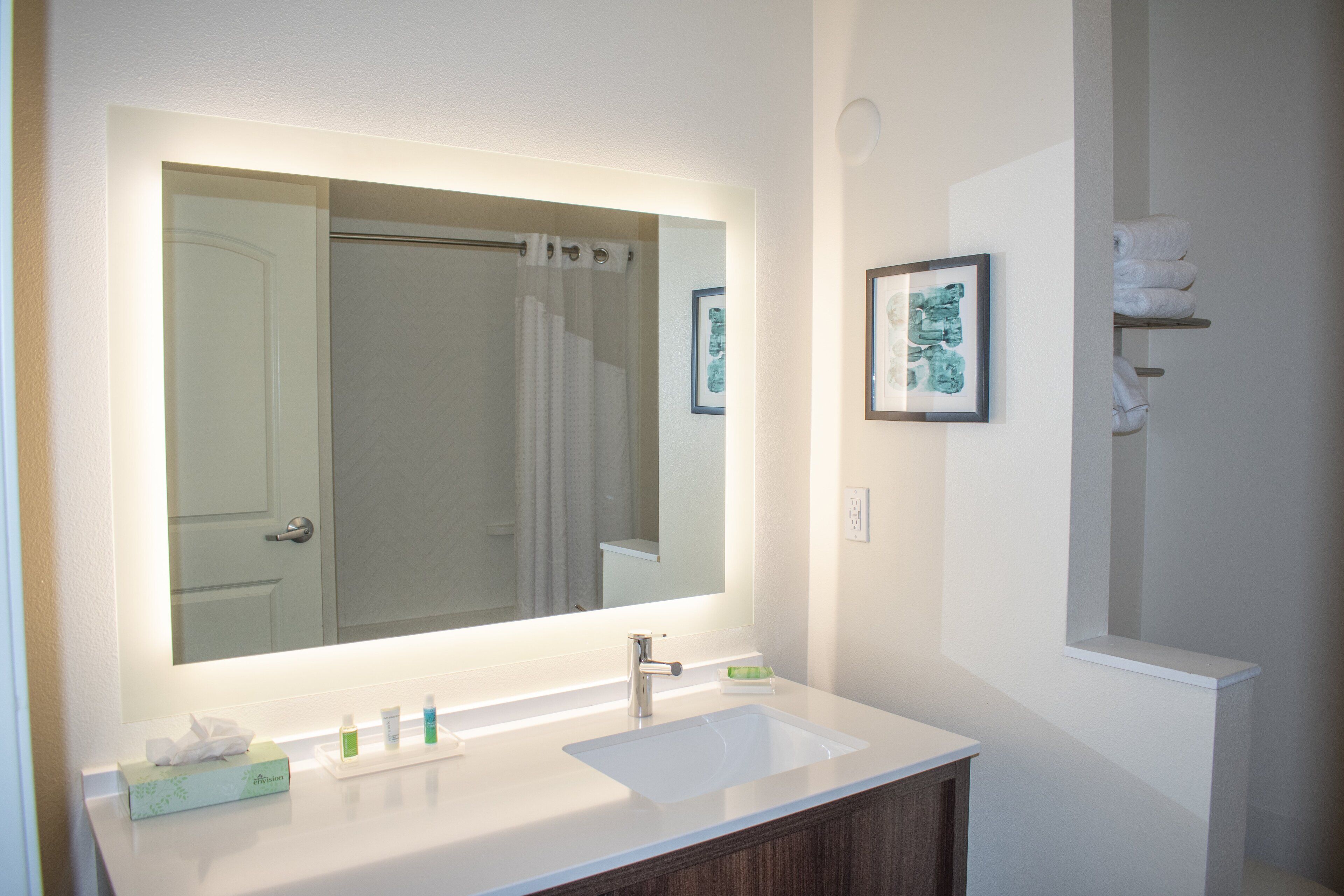 Une salle de bain avec un grand miroir, un lavabo blanc et un meuble-lavabo en bois.