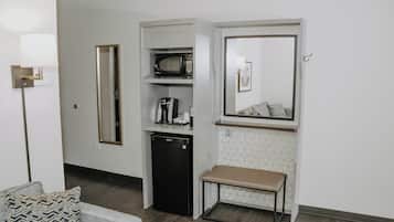 A compact kitchenette with a microwave, coffee maker, and refrigerator, a bench, and a mirror above the counter.