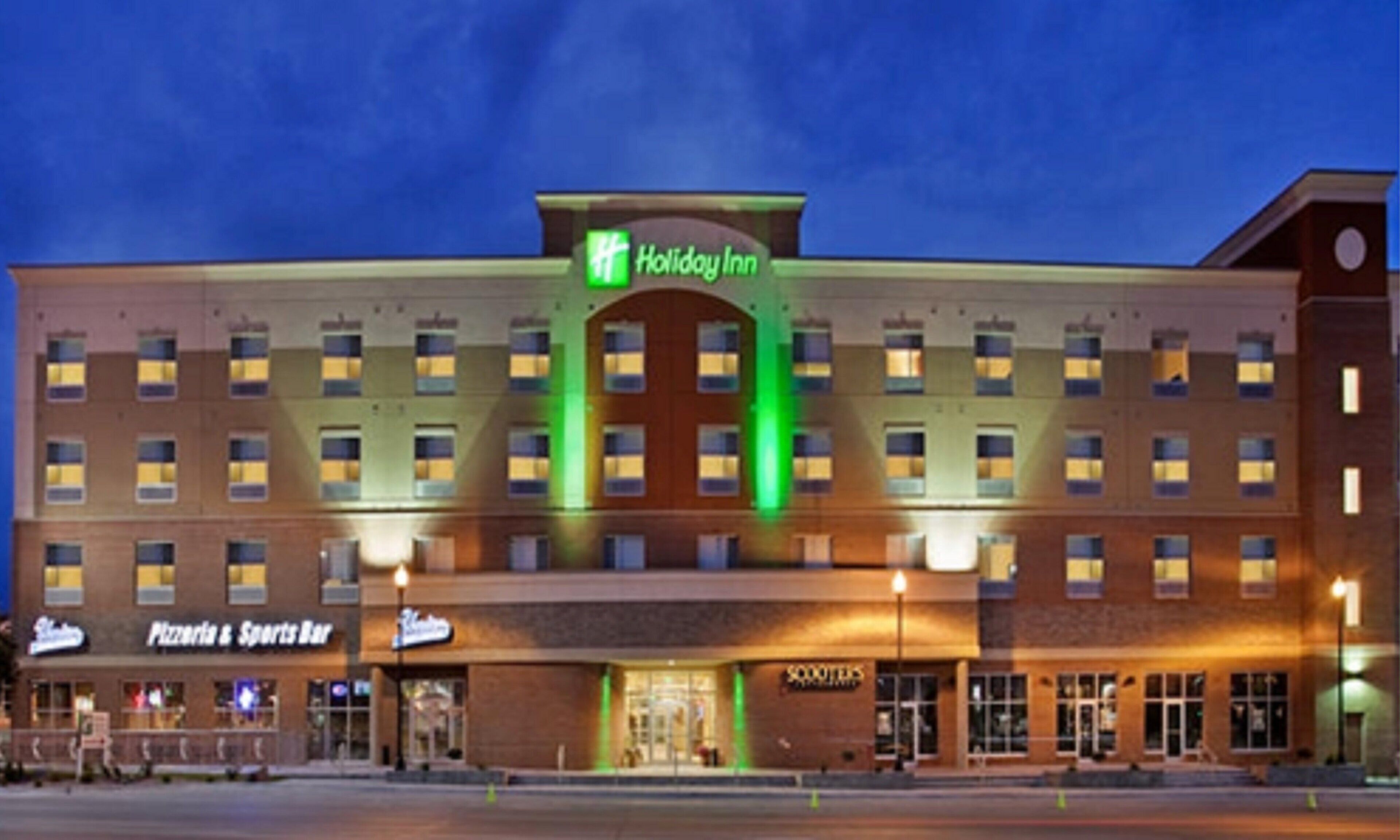 A Holiday Inn hotel with a central entrance, a Pizza & Sports Bar, and multiple floors with uniform window patterns.