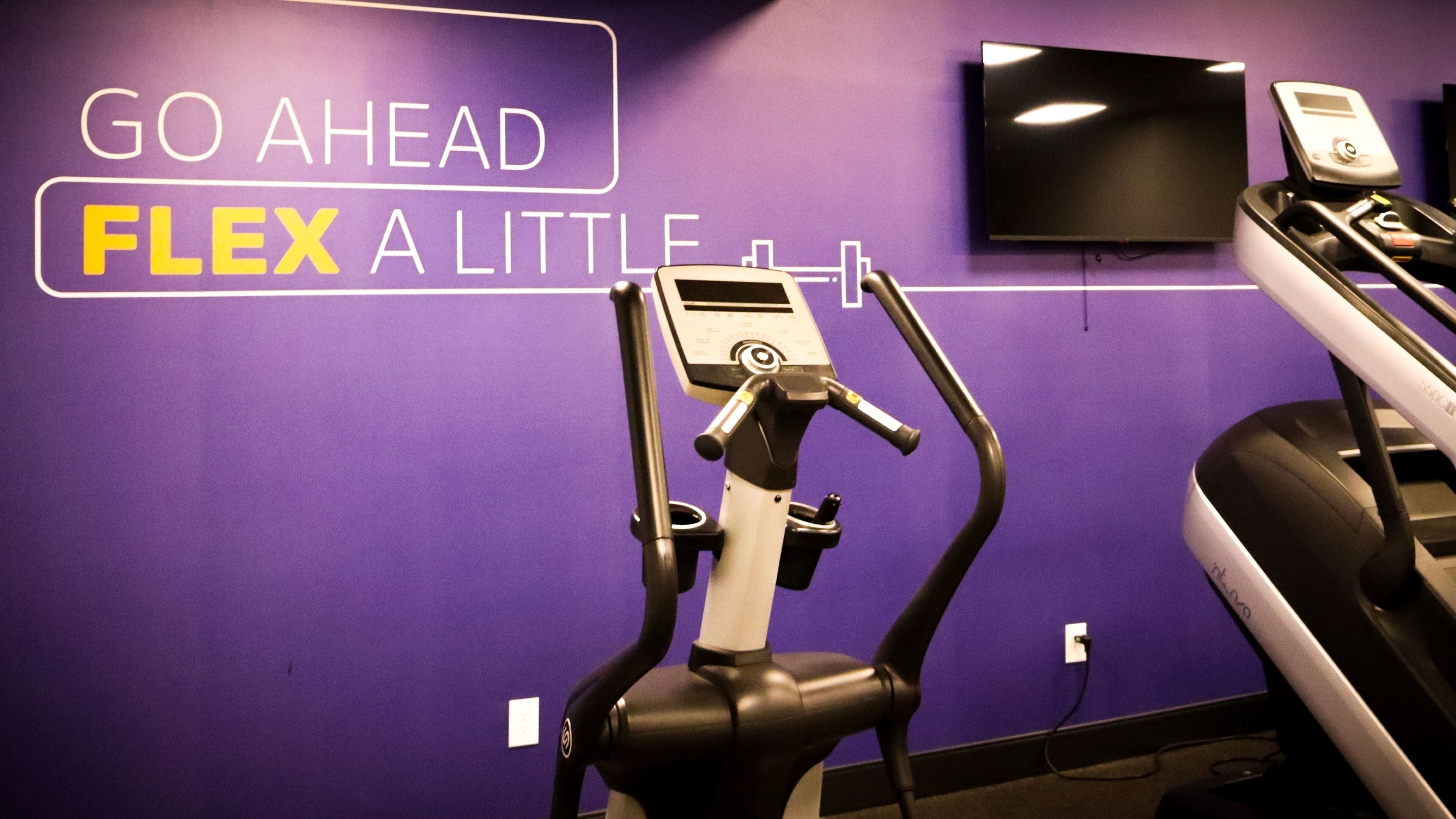 A gym with purple walls, a treadmill, and an elliptical machine.