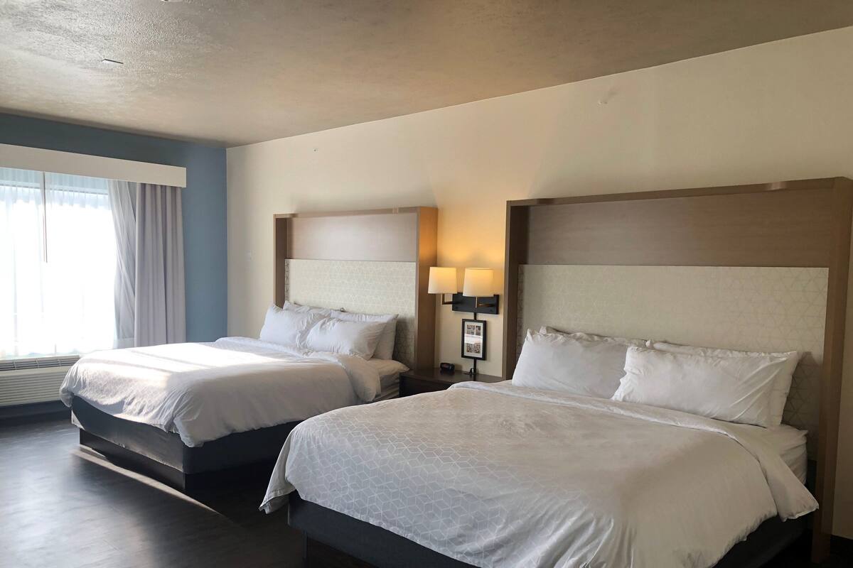 Una habitación de hotel con dos camas, una mesita de noche con lámpara y una ventana con cortinas.