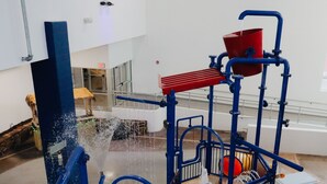 A water play area with a blue structure, a red bucket, and a basketball hoop. - Holiday Inn Omaha Downtown - Waterpark by IHG (Omaha)