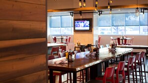 A restaurant with wooden walls, red chairs, a long dining table, hanging light fixtures, and a TV screen. - Holiday Inn Omaha Downtown - Waterpark by IHG (Omaha)