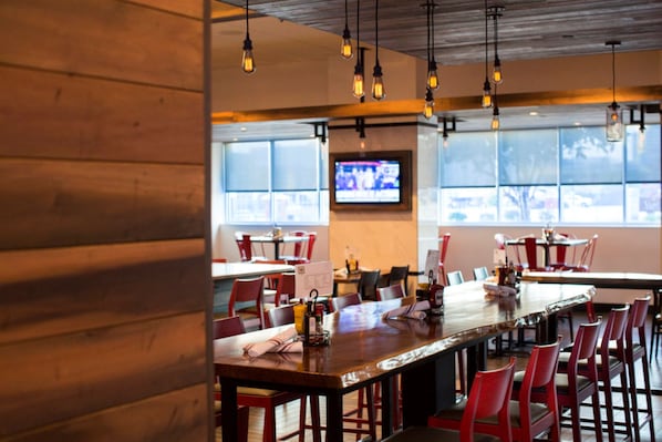 Un restaurante con paredes de madera, sillas rojas, una larga mesa de comedor, lámparas colgantes y una pantalla de televisión.