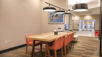 A conference room with a long table, orange chairs, a computer, and a painting on the wall.