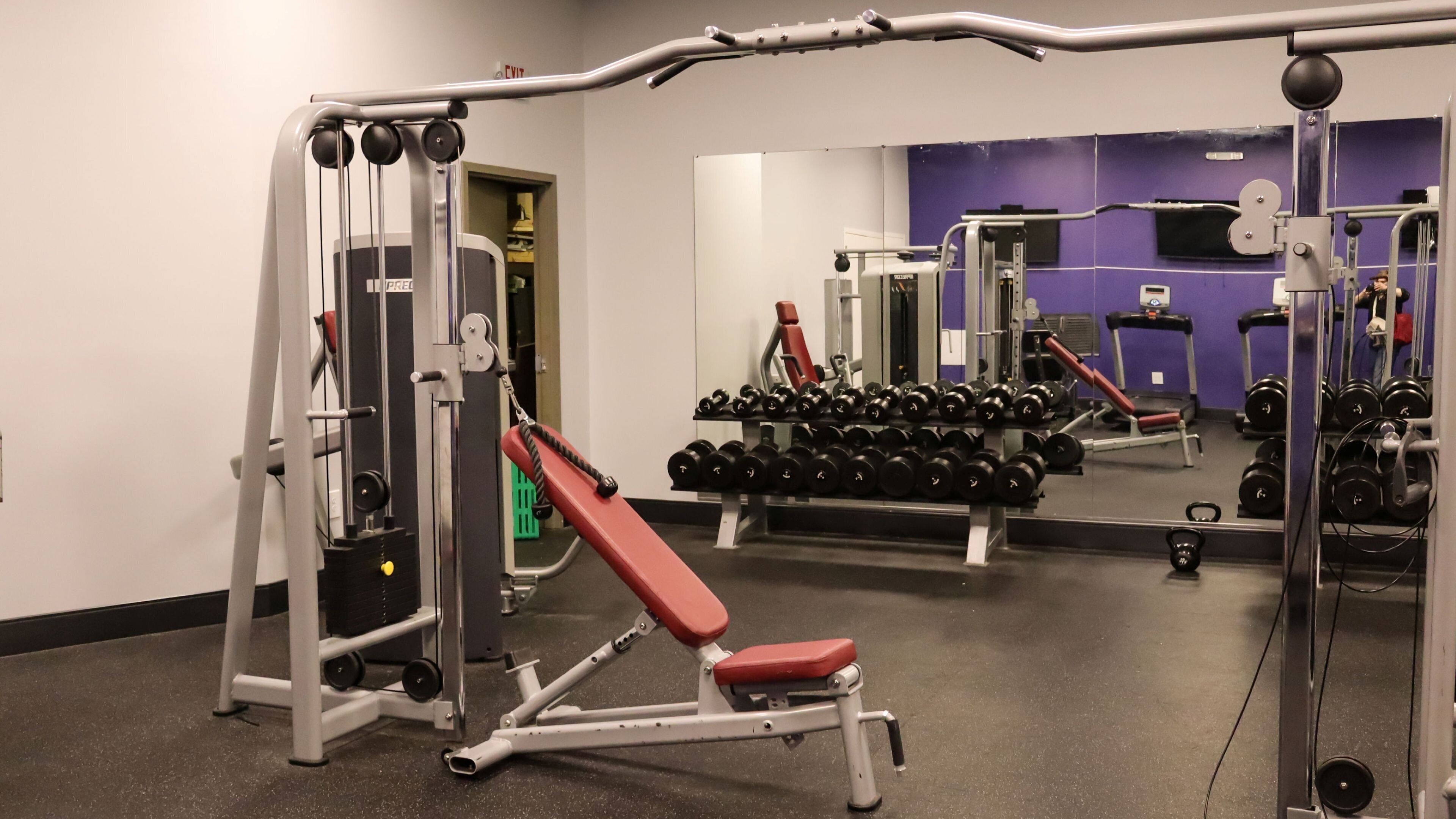 A gym with a bench, weight machines, and a mirror.