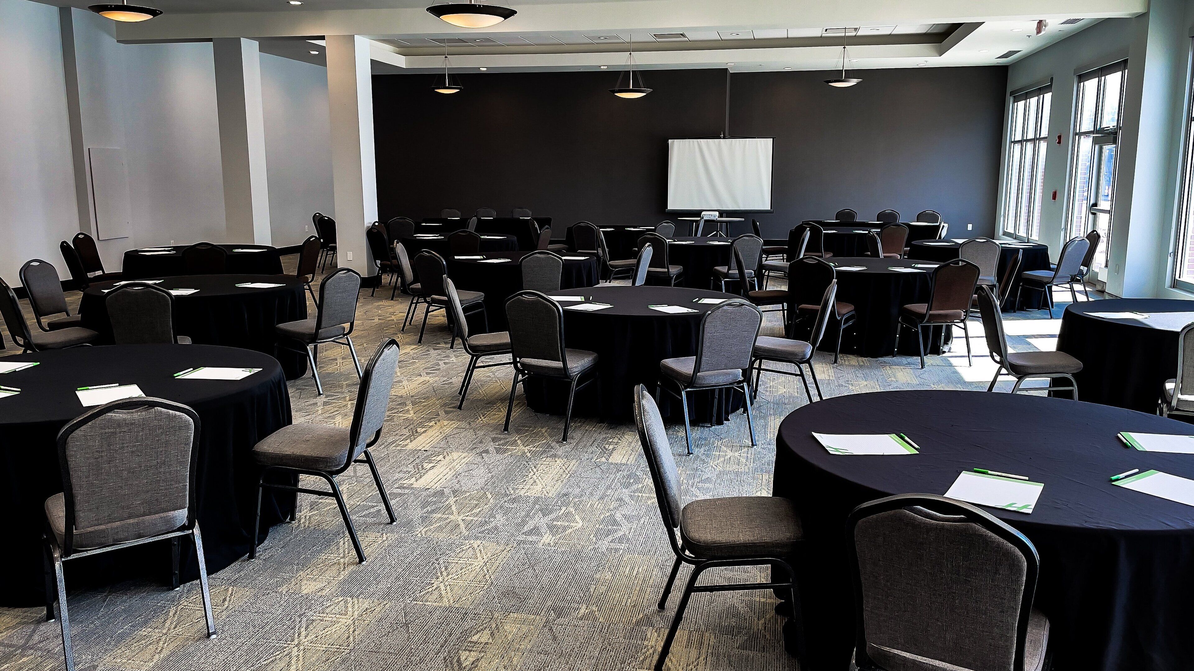 A conference room with multiple round tables and chairs, a whiteboard, and large windows.