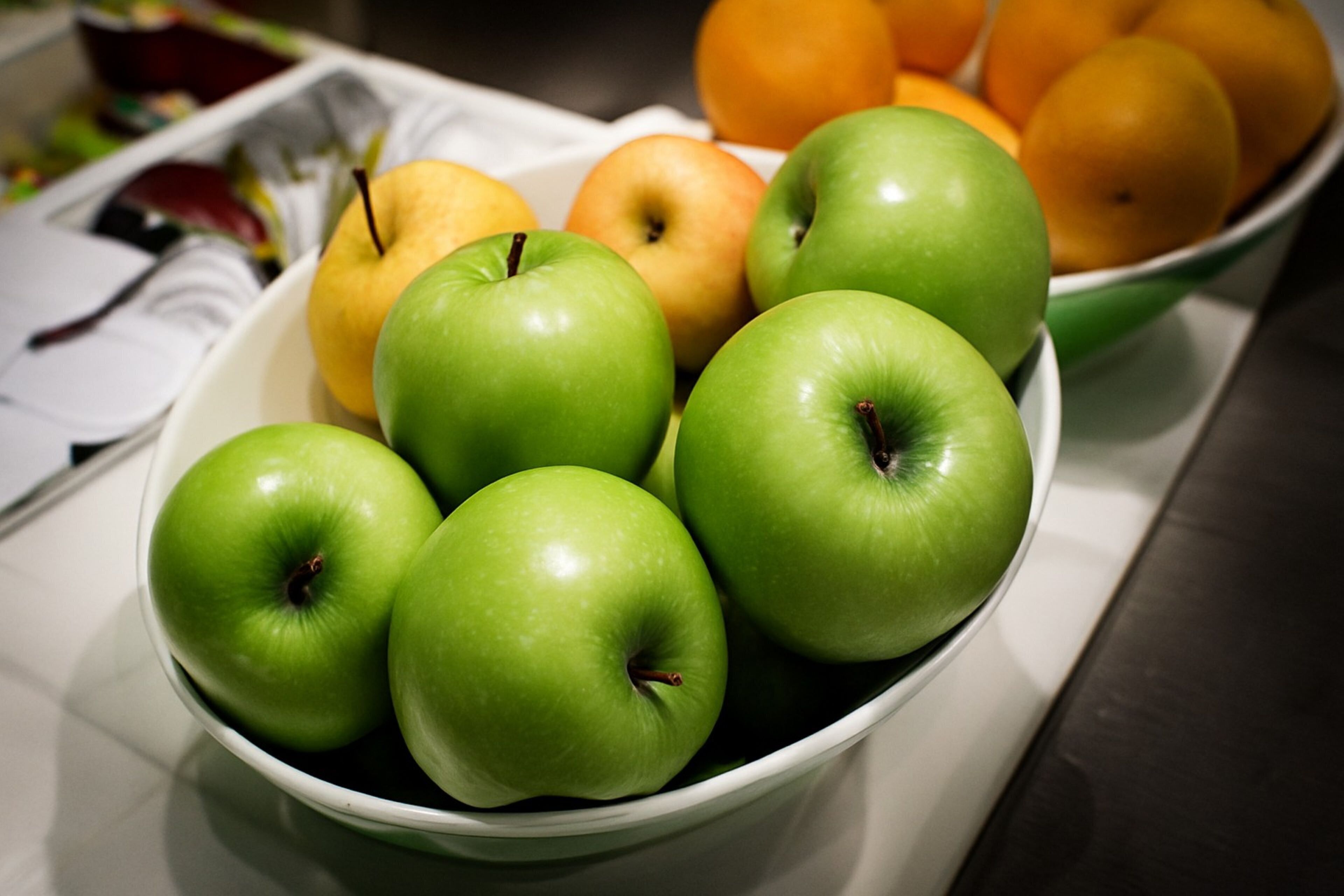 Un cuenco con manzanas verdes y naranjas sobre una mesa.