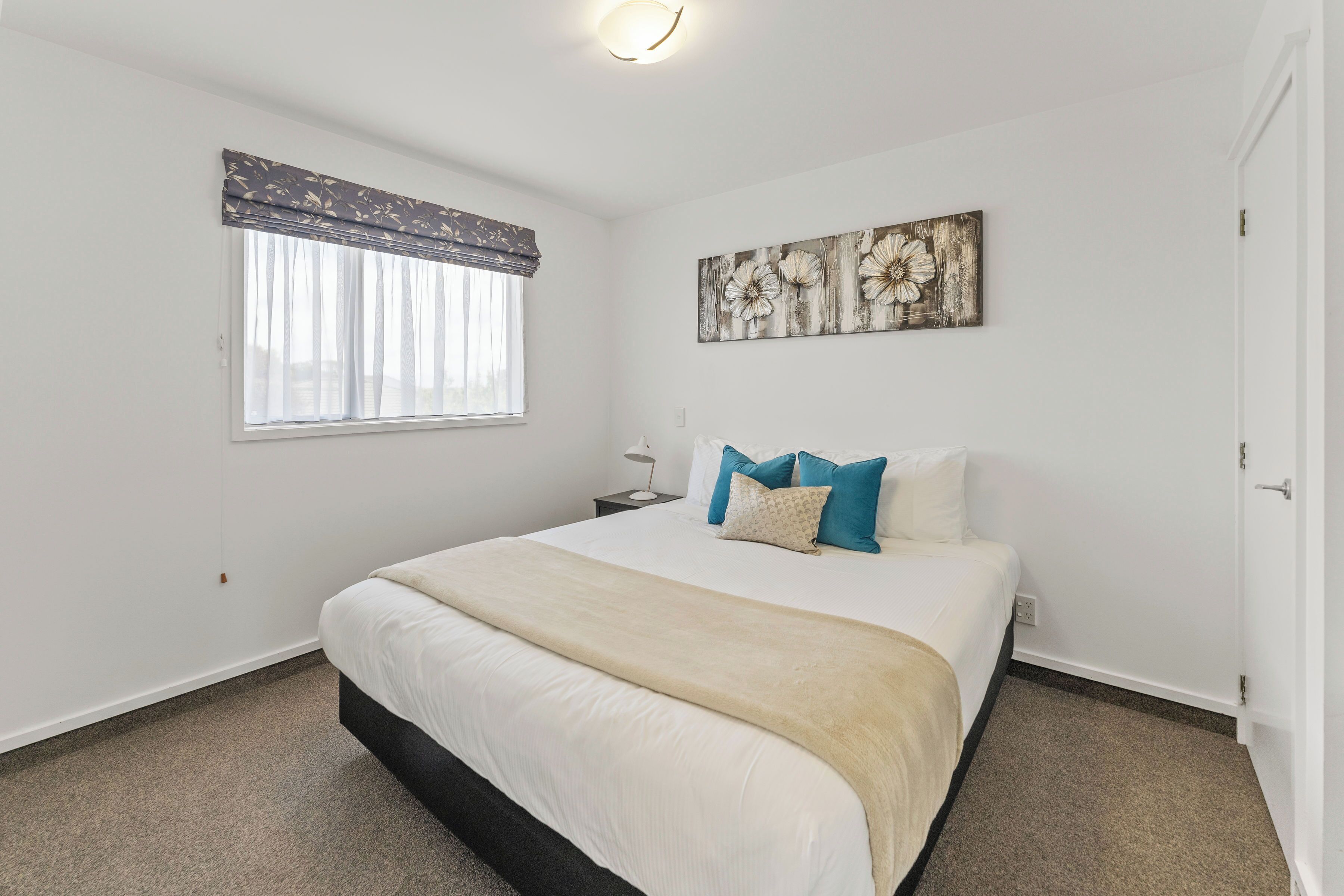 A bedroom with a large bed, a nightstand, a wall-mounted artwork, and a window with curtains.